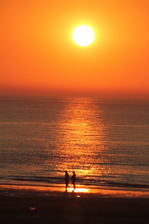 A couple walking on the beach while the sun is setting